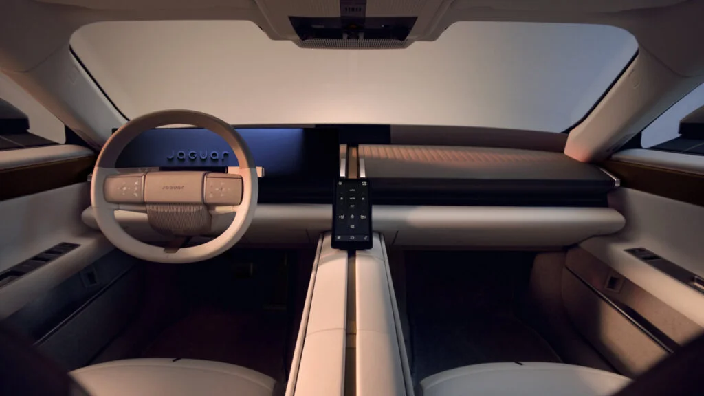 Jaguar Type 01 interior with an oval steering wheel, a wide driver’s display and a small portrait control screen on the central spine between two pale seats