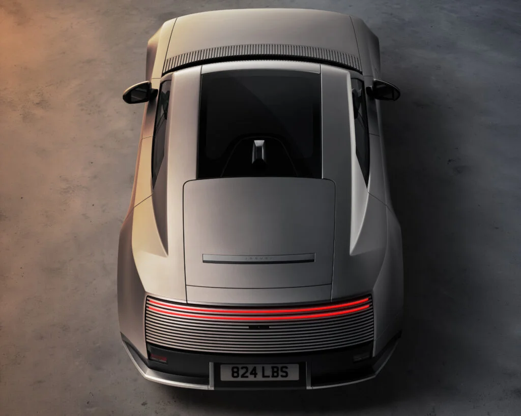 Rear of a silver Jaguar Type 01 seen from above, showing its glass roof panel, curved rear wings and a red light bar set into the slatted rear panel