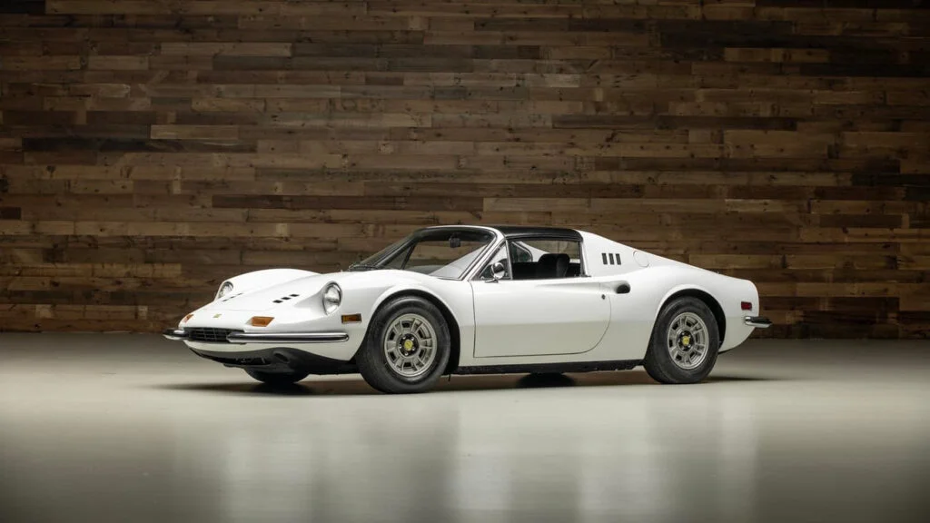 White Ferrari Dino 246 GTS with its targa roof panel removed, photographed in a studio in front of a wall of reclaimed wooden boards