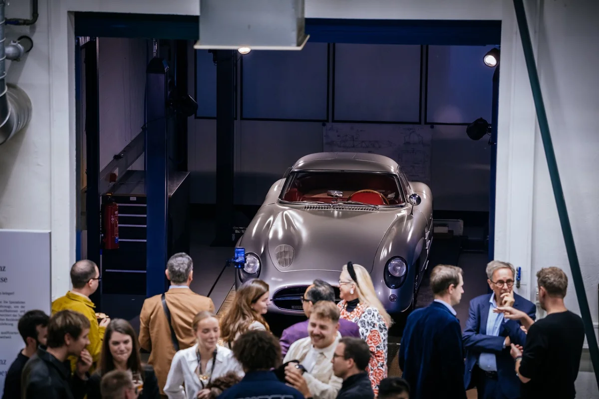 Silver Mercedes-Benz 300 SLR Uhlenhaut Coupé raised on a lift behind a crowd of guests at the Classic Center reopening