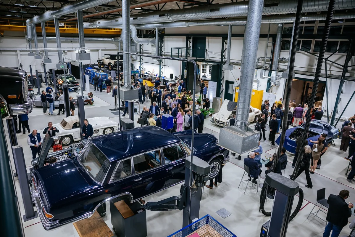 Elevated view of a dark blue Mercedes-Benz 600 on a lift in the Classic Center workshop, with guests mingling among other classic Mercedes-Benz cars at the opening