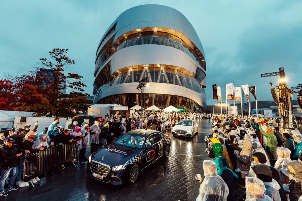Black Mercedes-Benz S-Class driving through crowds in rain ponchos outside the Mercedes-Benz Museum in Stuttgart