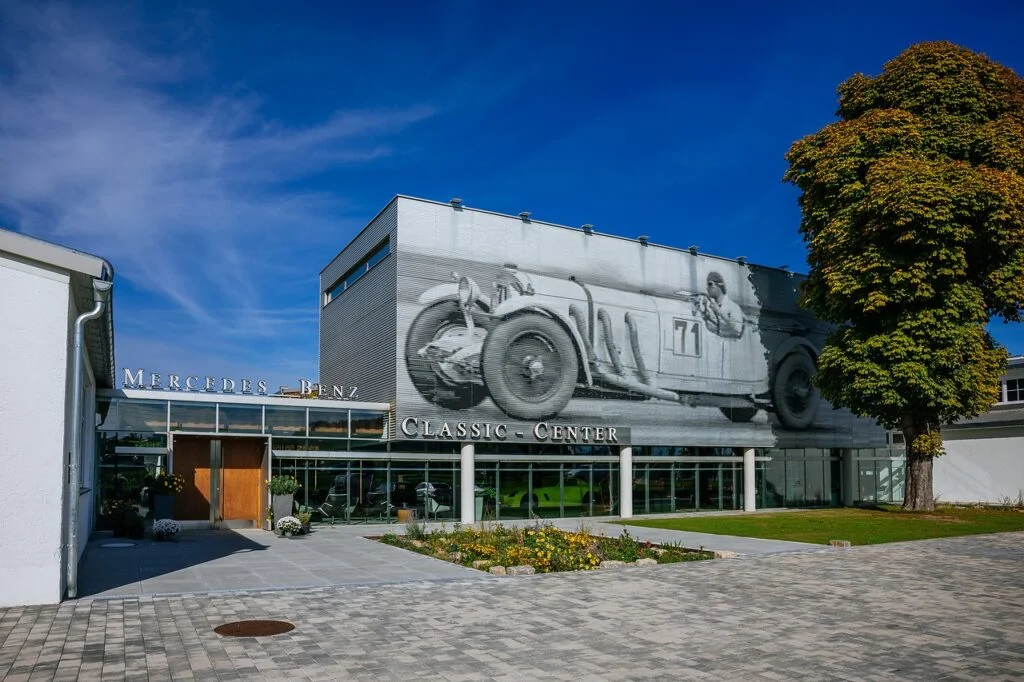 Exterior of the Mercedes-Benz Classic Center in Fellbach, with a large mural of a pre-war Mercedes-Benz racing car on the building above the entrance