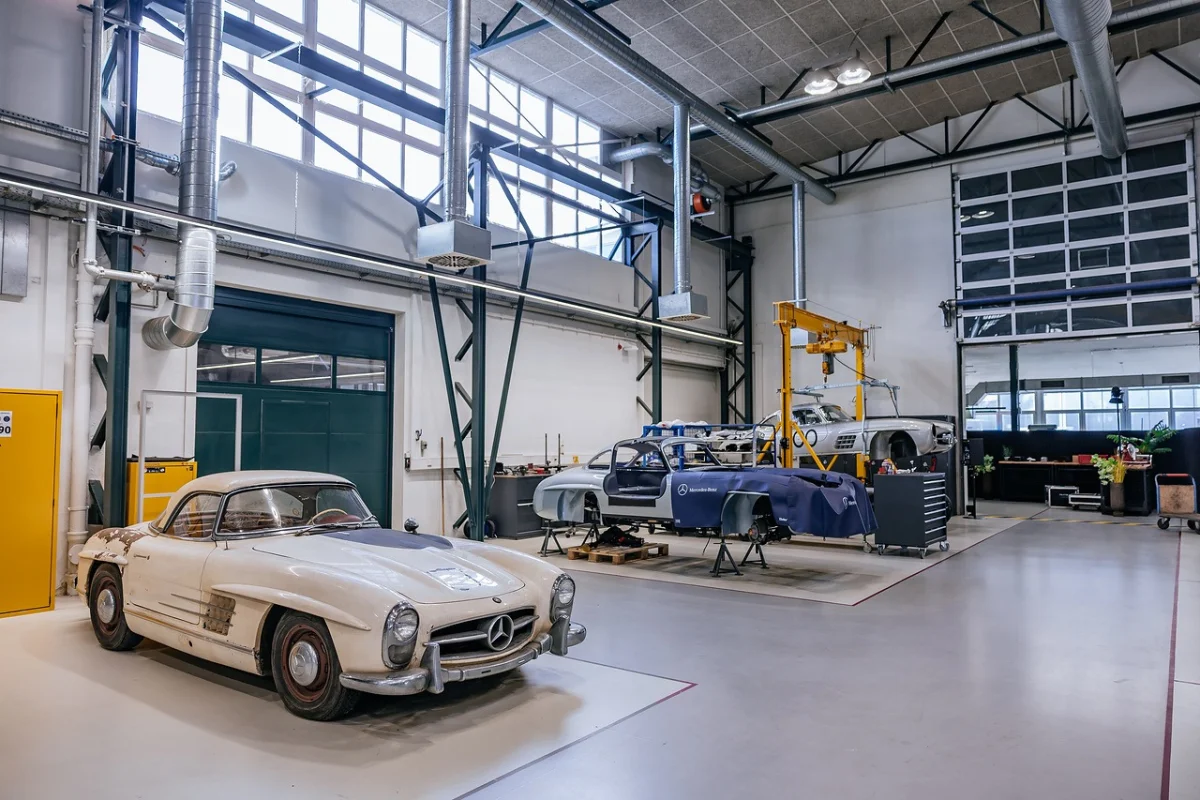 Unrestored white Mercedes-Benz 300 SL with a hardtop in the Classic Center workshop, with 300 SL bodyshells under restoration in the background